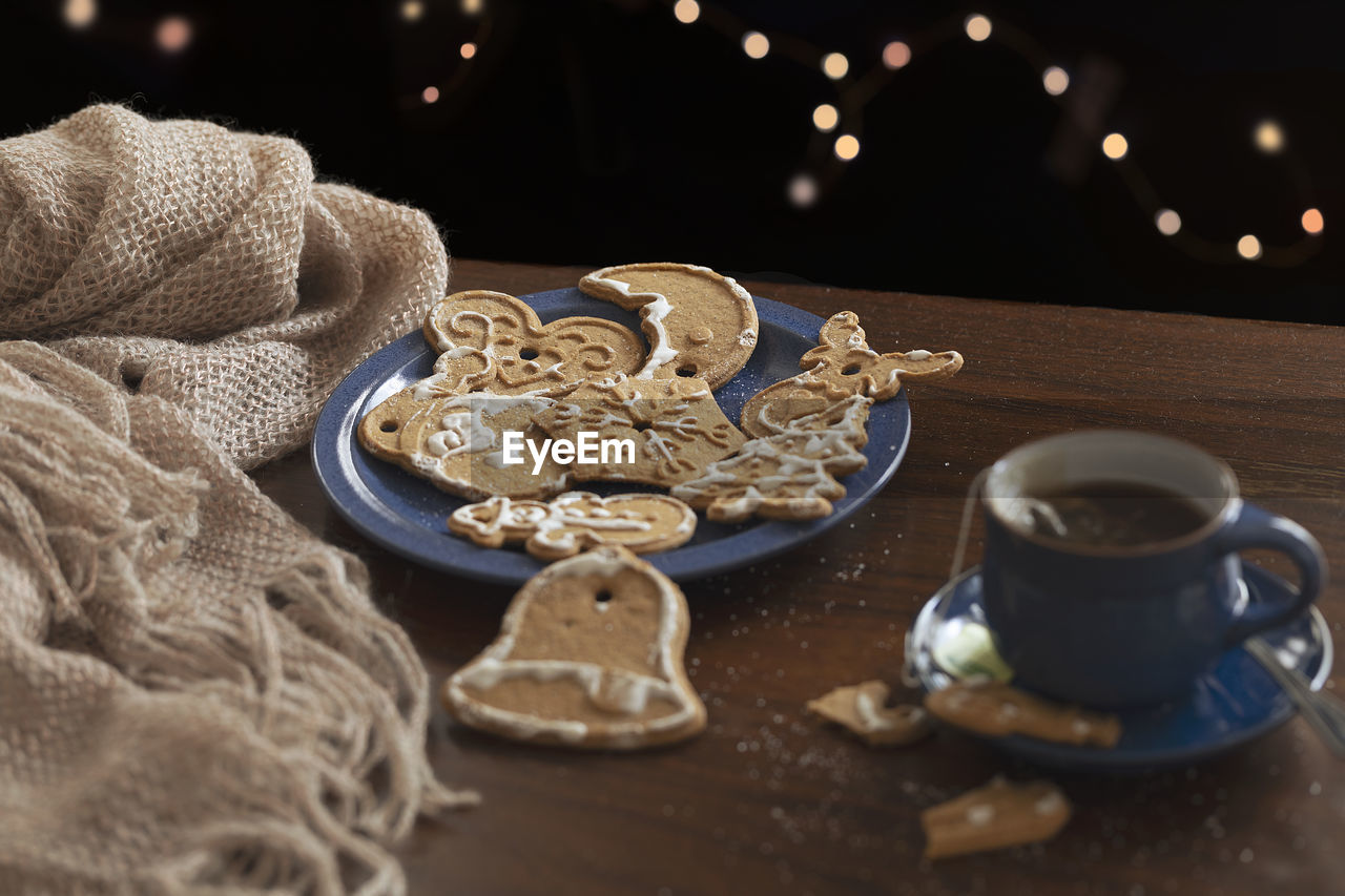 A table with spiced christmas cookies, a woolen scarf and a cup. lights bokeh in background. 