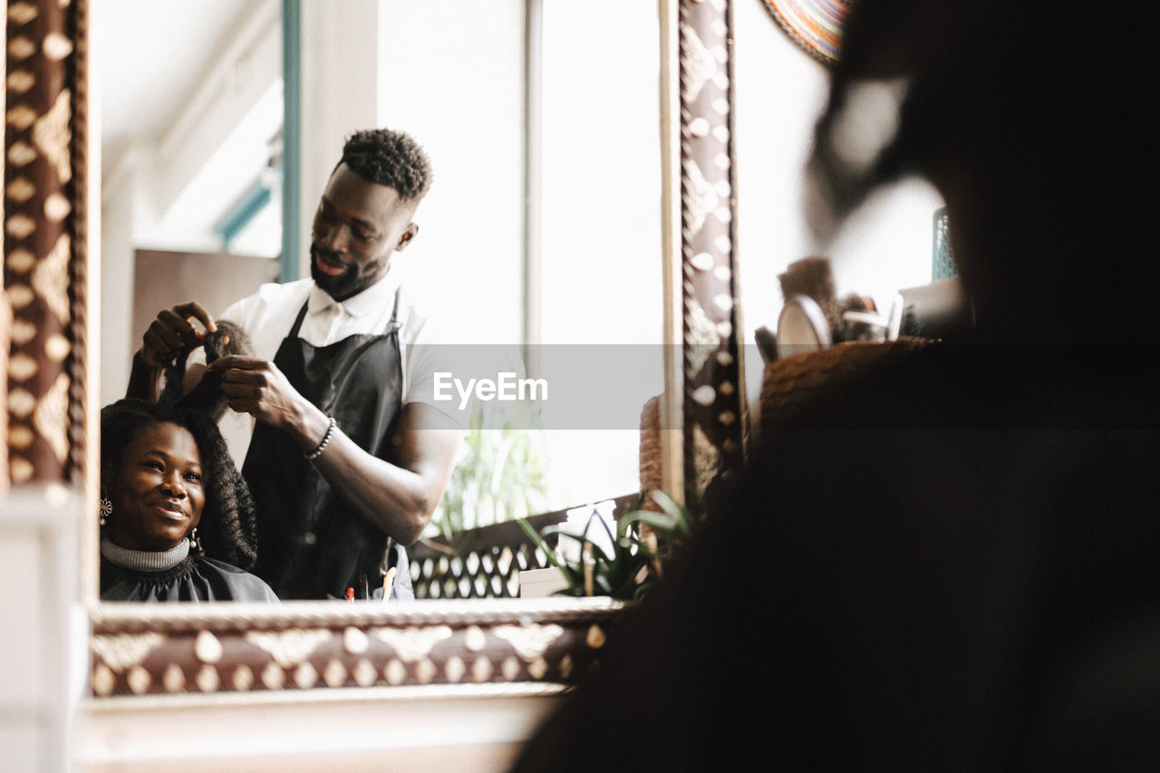 Male hairdresser making locs of female customer at barber shop