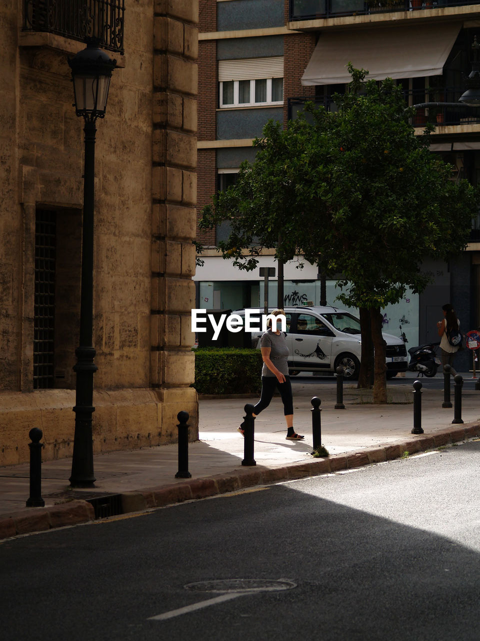 urban area, road, architecture, street, city, built structure, building exterior, downtown, men, adult, full length, city life, lifestyles, transportation, infrastructure, tree, day, nature, leisure activity, walking, neighbourhood, city street, women, lighting, group of people, pedestrian crossing, plant, outdoors, lane, building, town square, shadow, motion, sports