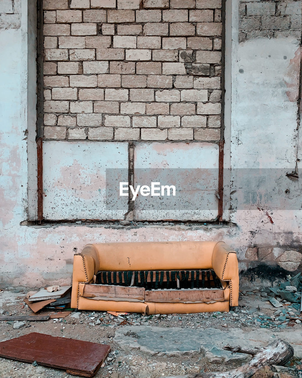 Abandoned sofa against brick wall of old building