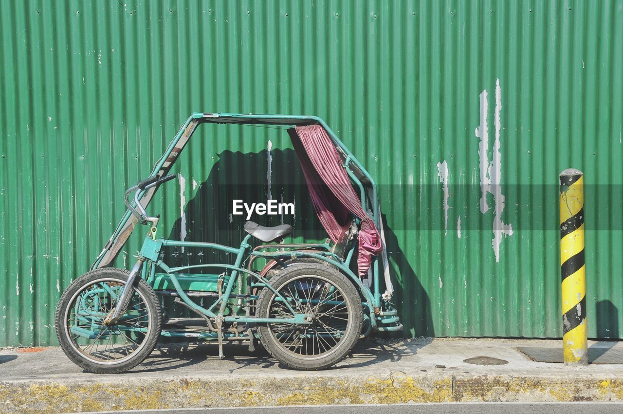 Tricycle parked by corrugated iron