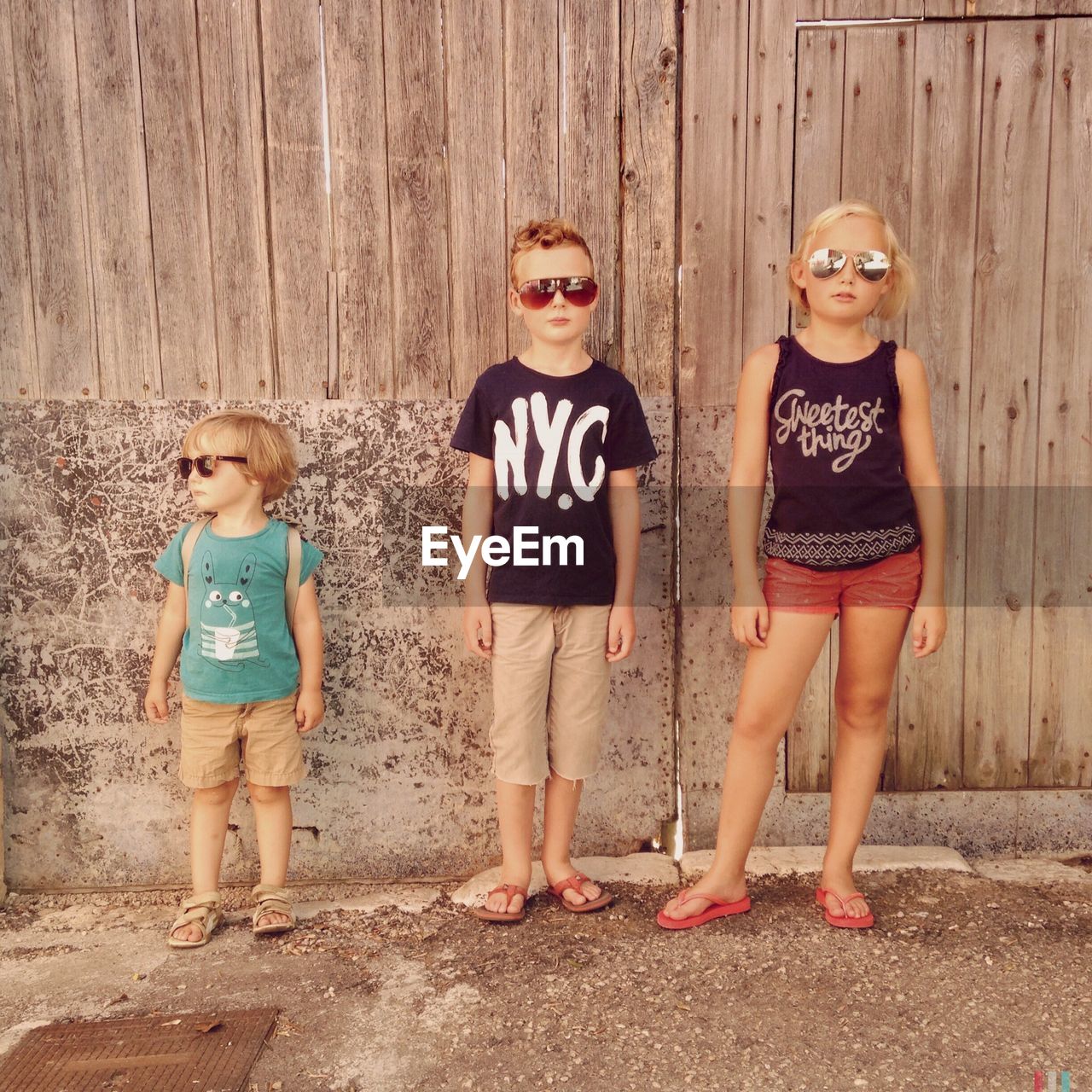 Portrait of siblings standing against wooden fence