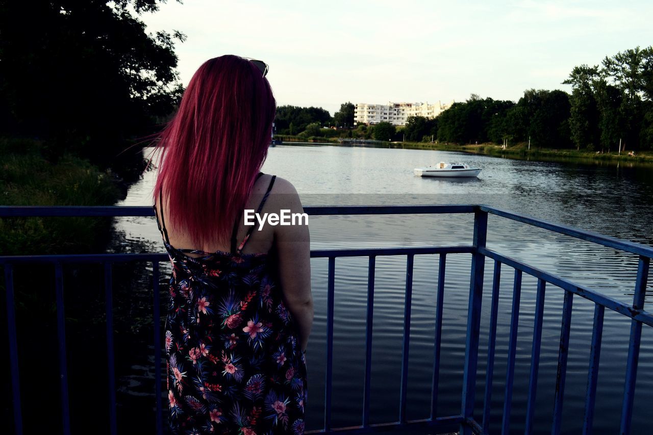 REAR VIEW OF WOMAN LOOKING AT RIVER AGAINST BUILDINGS