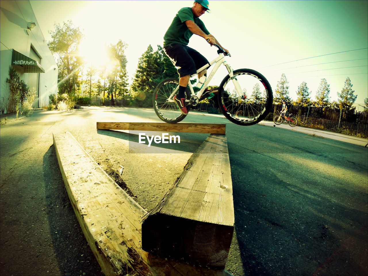 Full length of man riding bicycle on wooden planks over road against clear sky