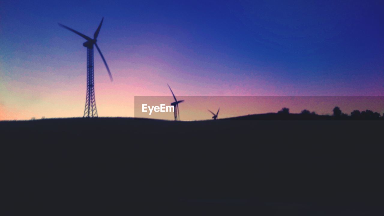 SILHOUETTE OF WIND TURBINES ON FIELD AT DUSK