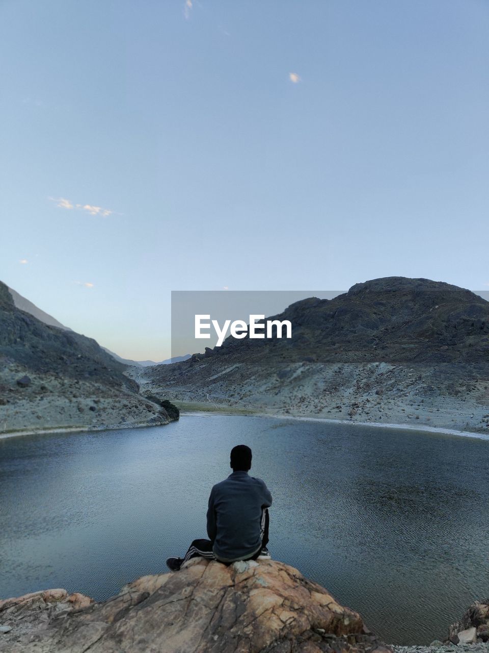 Rear view of man sitting on rock by mountain against sky