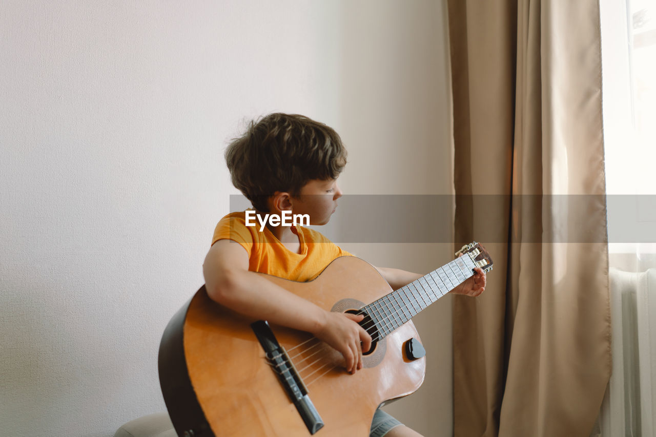 Cute boy learns to play the classical guitar in home. cozy home.