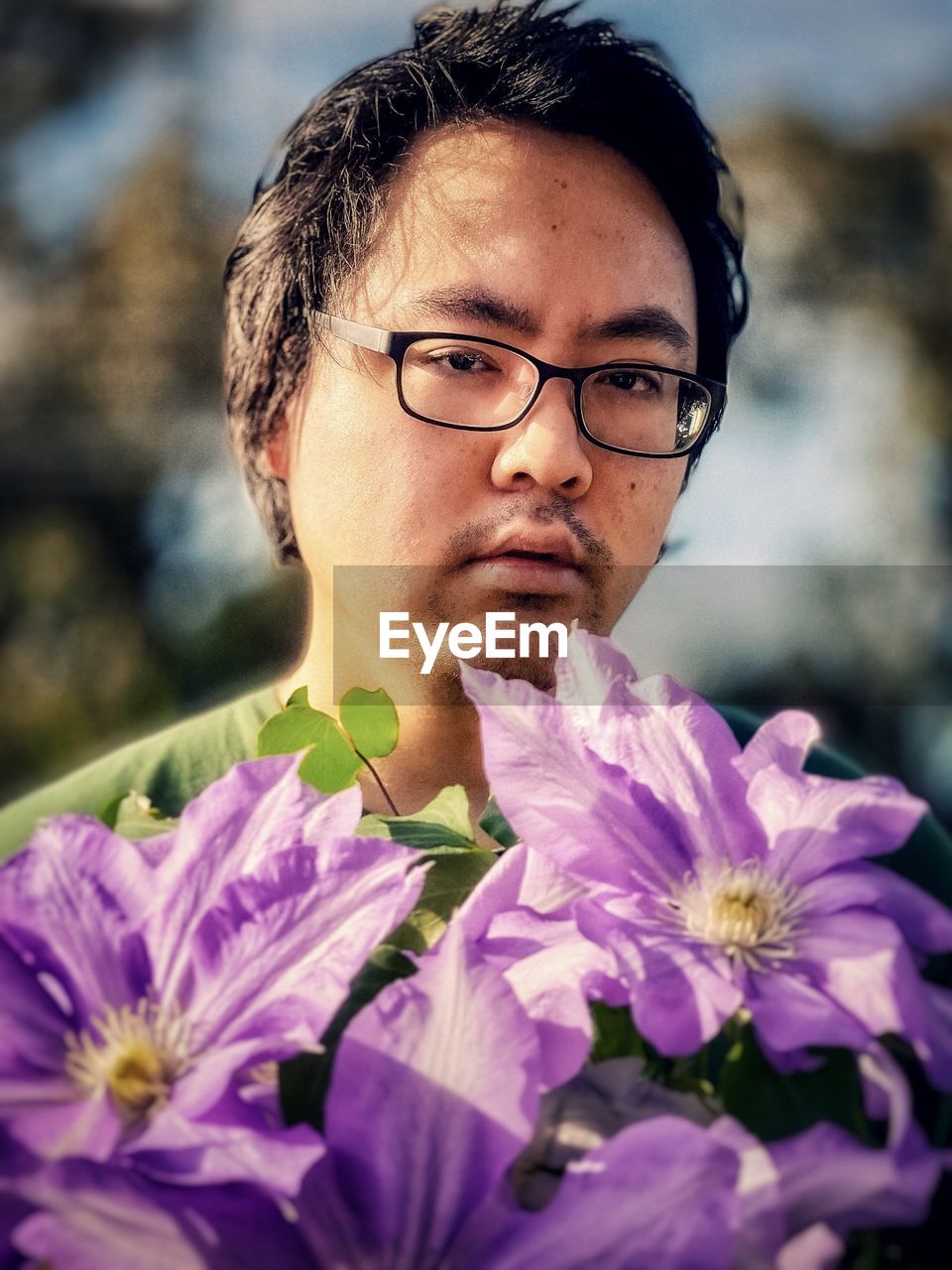 Close-up portrait of young man with large, purple clematis flowers.