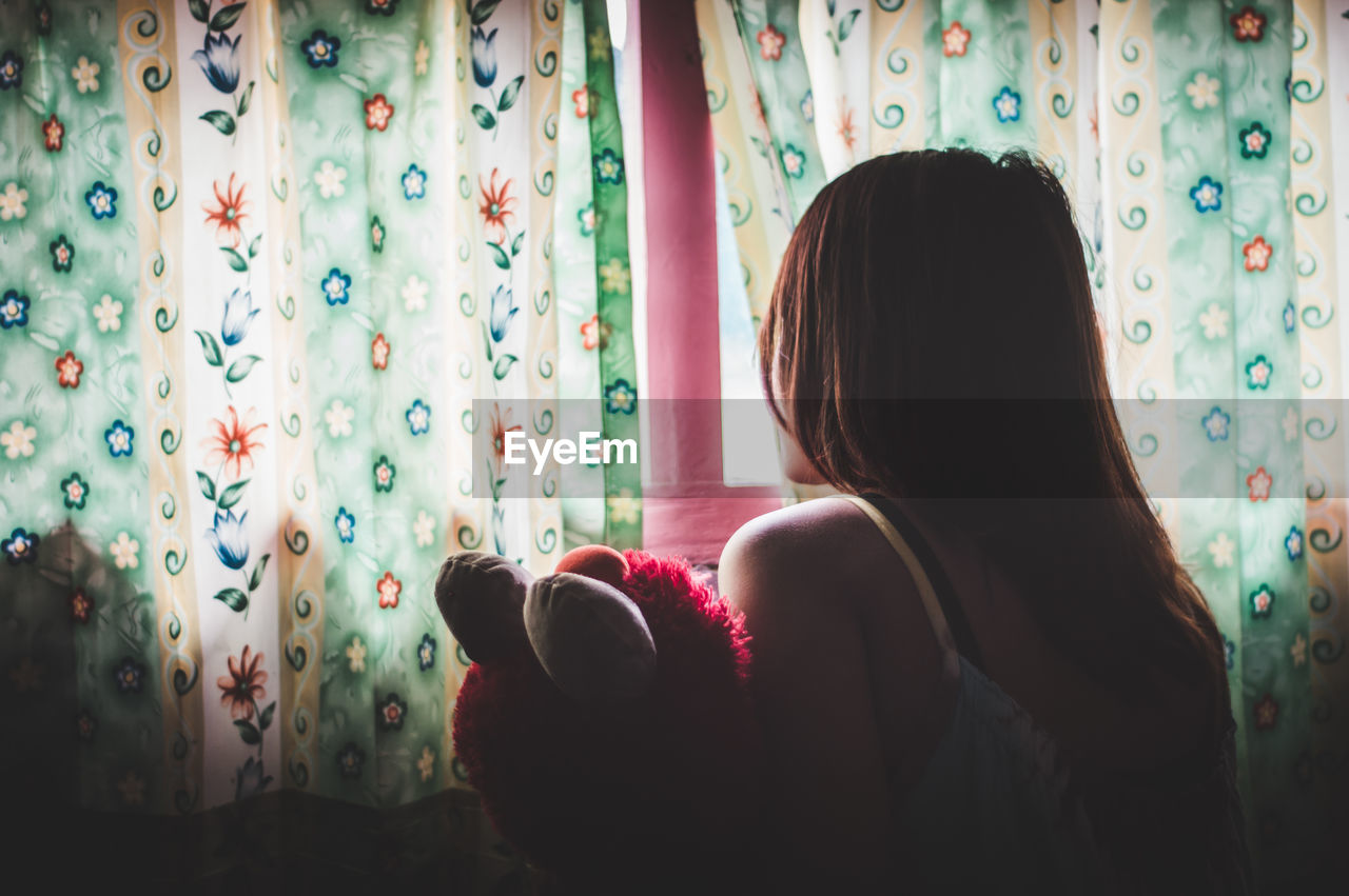 Rear view of woman looking through window at home