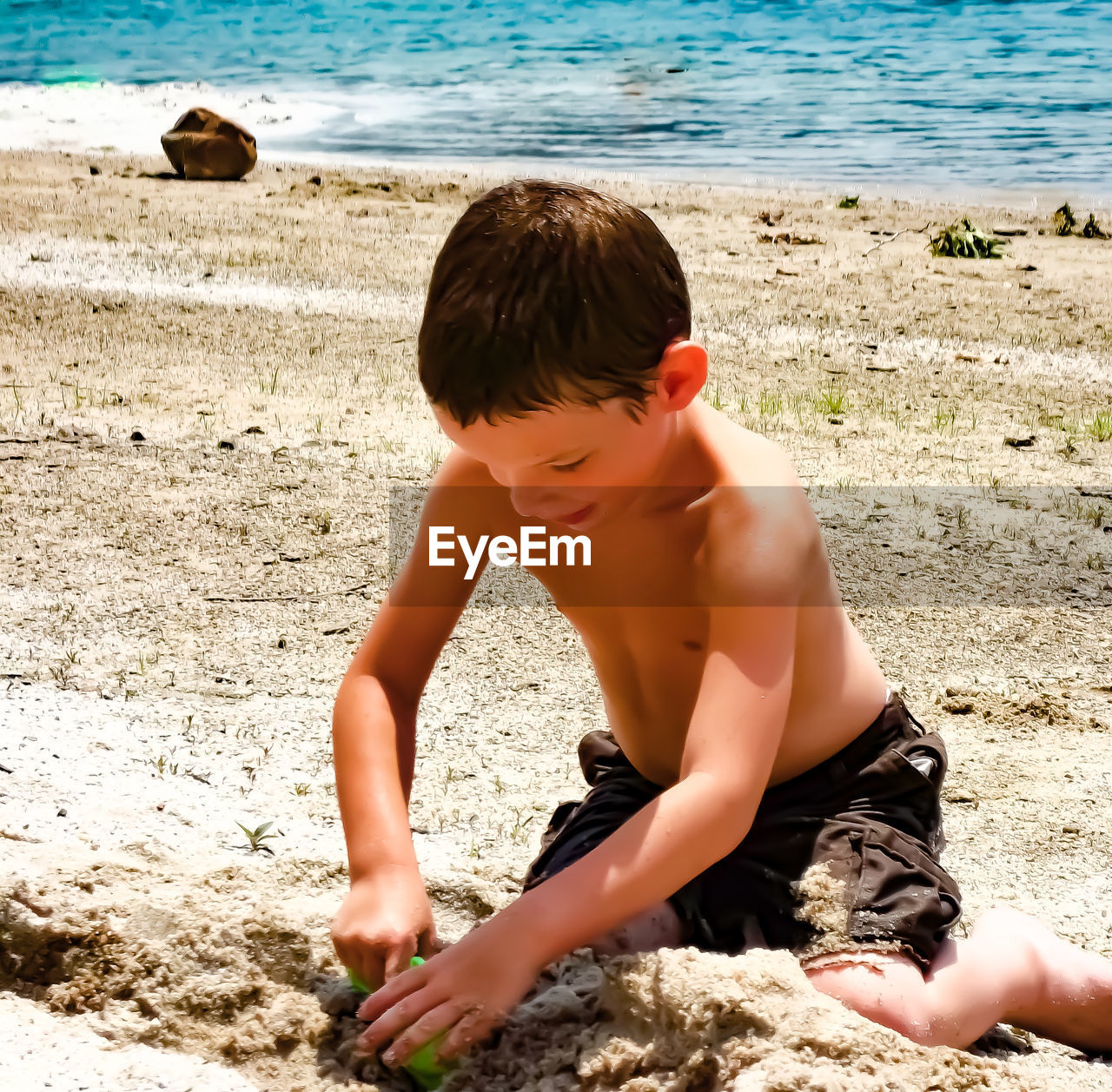 Shirtless boy playing with sand on beach