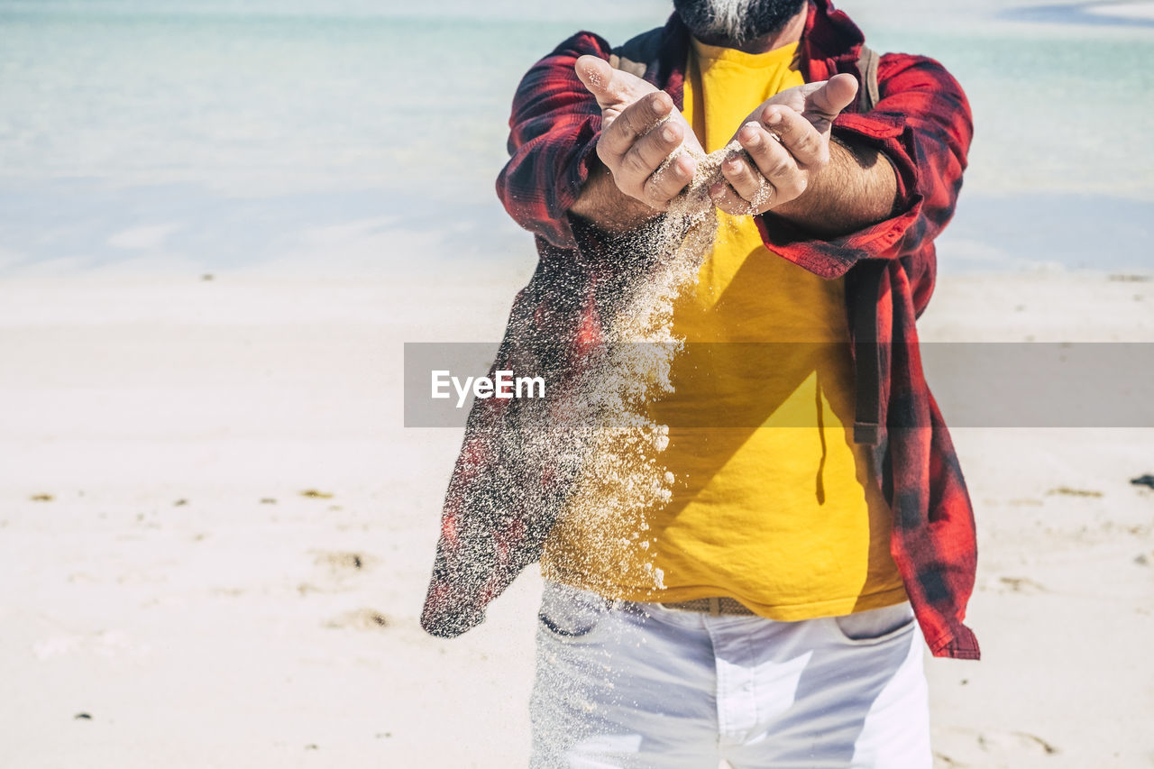 Midsection of man pouring sand at beach