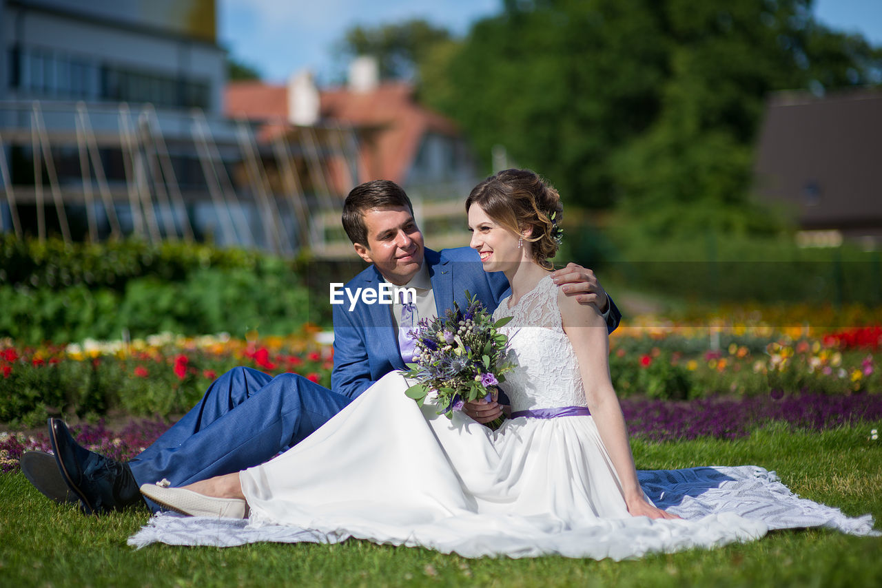 Bride and bridegroom sitting on picnic blanket at park