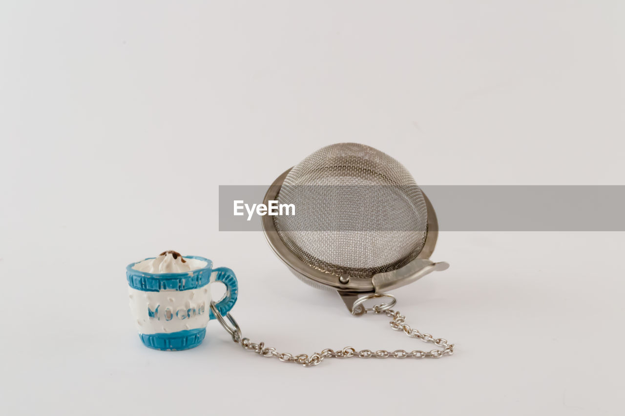 Close-up of strainer and cup over white background