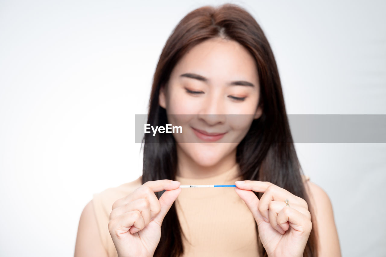 one person, smiling, women, portrait, happiness, young adult, adult, hand, holding, long hair, emotion, human face, finger, studio shot, front view, hairstyle, indoors, cheerful, positive emotion, skin, person, human head, white background, headshot, photo shoot, human hair, relaxation, human mouth, human eye, looking at camera, teeth, smile, lifestyles, portrait photography, cut out, cute, enjoyment, brown hair, looking, casual clothing, nose, clothing, wellbeing, arm, joy, female, food and drink, copy space, lip