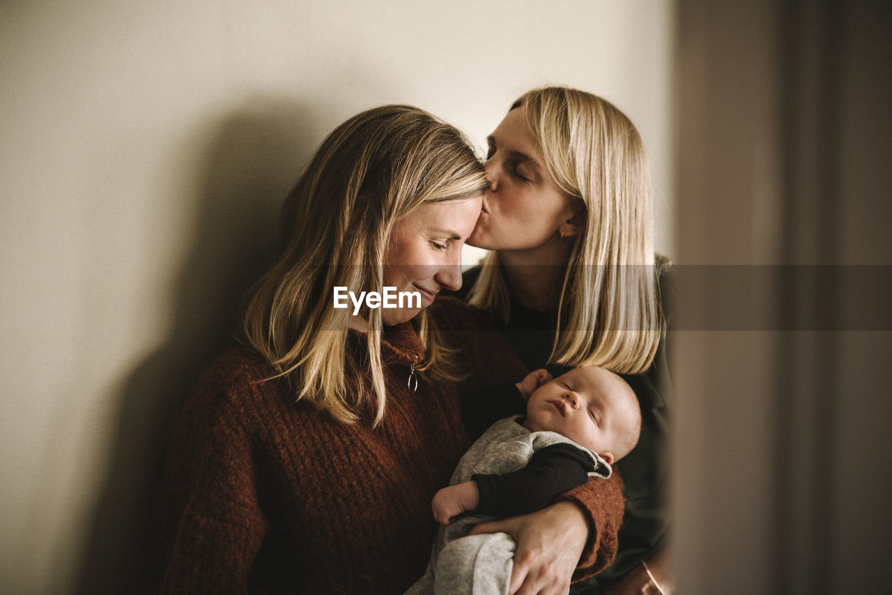 Mothers kissing and holding sleeping newborn baby