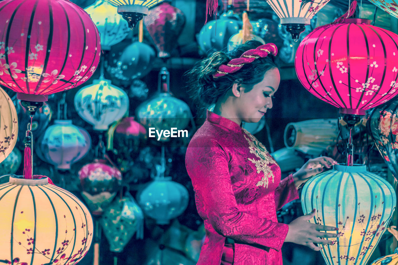 MIDSECTION OF WOMAN WITH BALLOONS AT ILLUMINATED LANTERNS