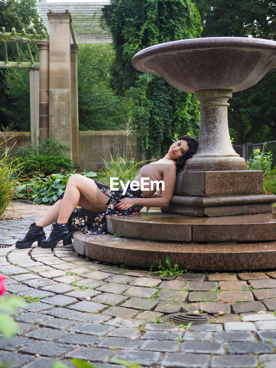 Woman sitting by fountain against trees