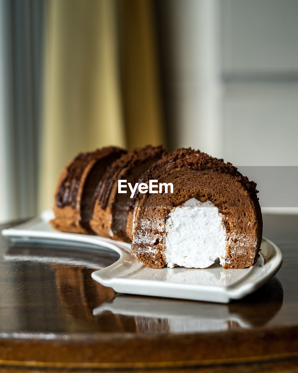 Chocolate roll with fresh cream on a white plate and wooden background