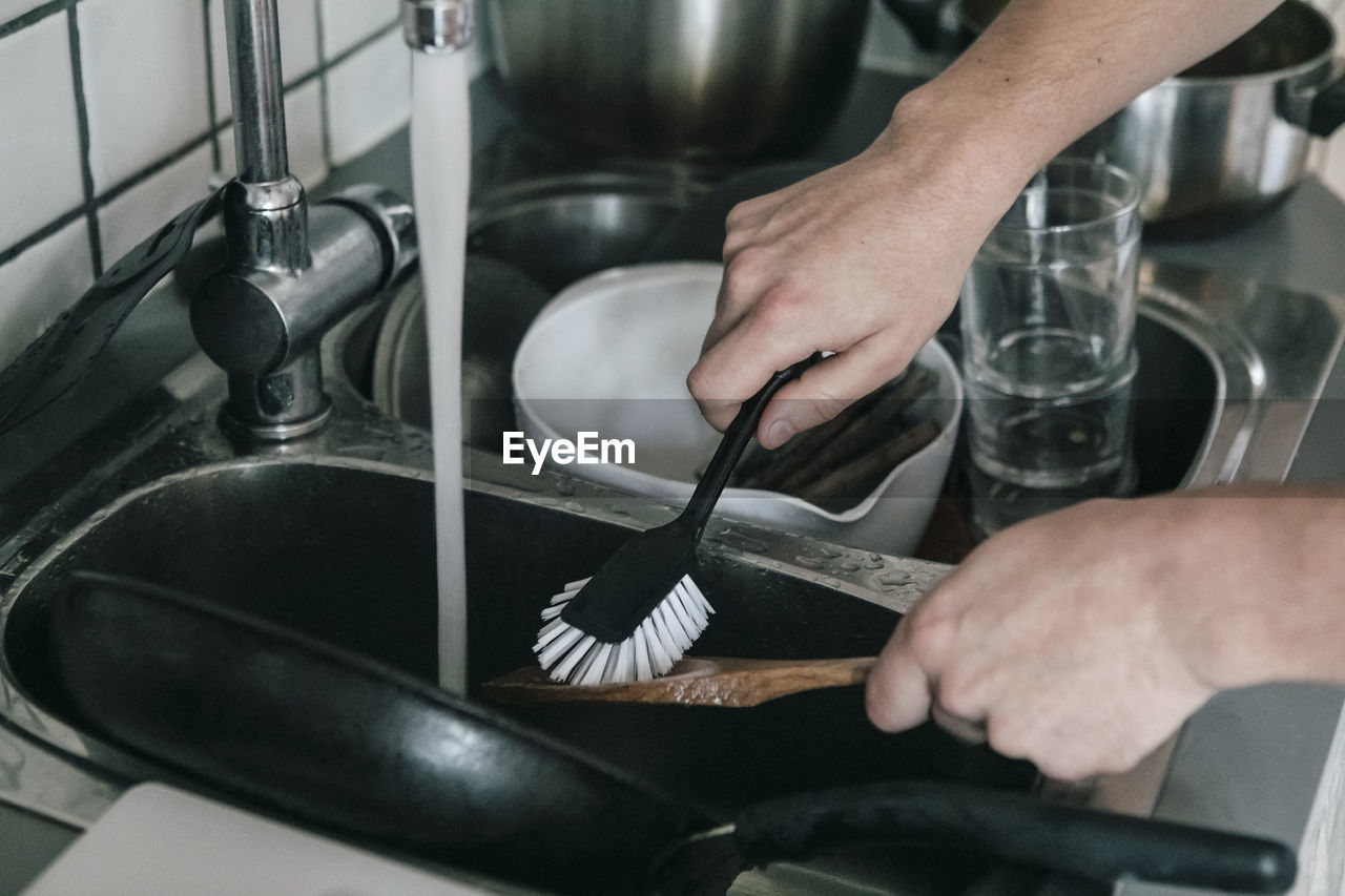 Cropped image of man washing wooden spoon with dish brush in sink at kitchen