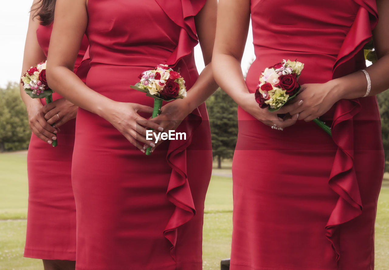 Midsection of bridesmaids holding bouquets in lawn