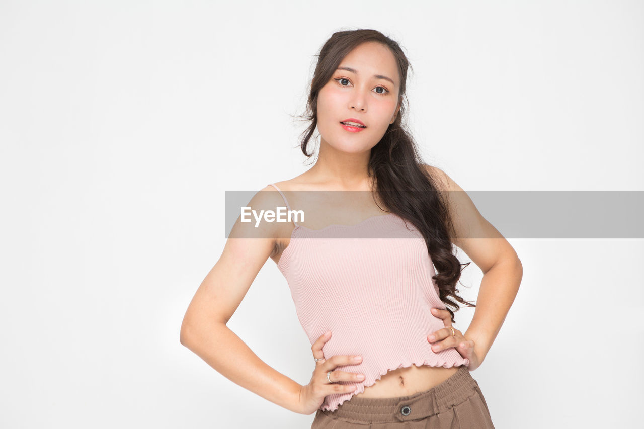 one person, studio shot, women, portrait, adult, young adult, indoors, looking at camera, clothing, photo shoot, hairstyle, white background, trunk, standing, hand on hip, long hair, undergarment, lifestyles, copy space, smiling, front view, fashion, brown hair, hand, waist up, happiness, sleeve, three quarter length, emotion, female, human leg, limb, cut out, arm