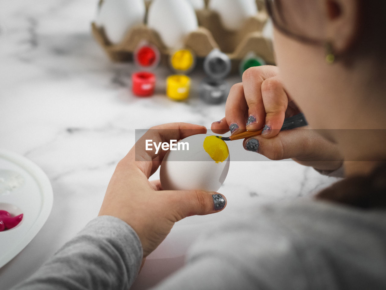 Little caucasian girl paints an easter egg with a brush with yellow acrylic pain