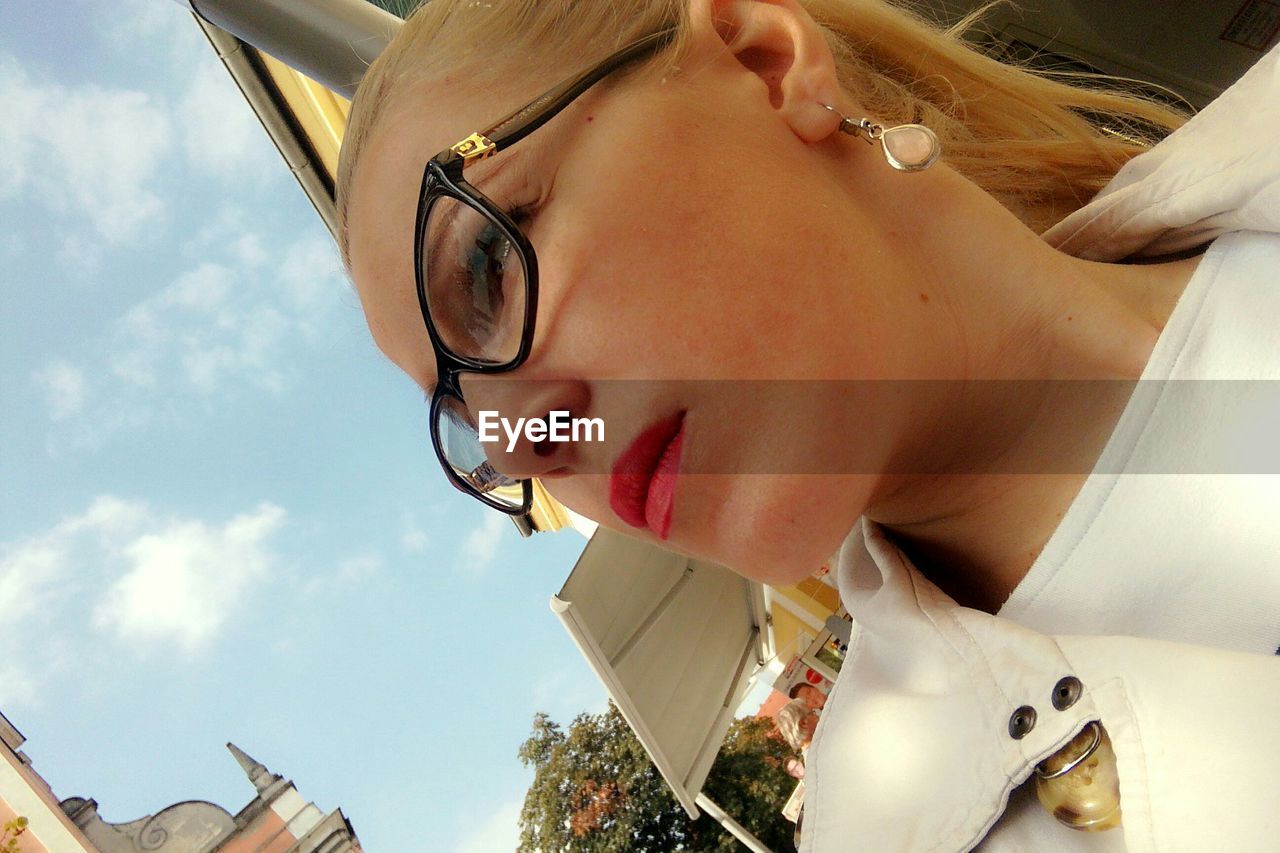 Tilt image of thoughtful woman wearing eyeglasses in city against sky