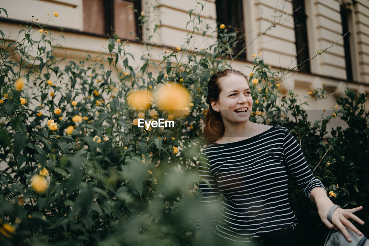 Smiling young woman standing by plants