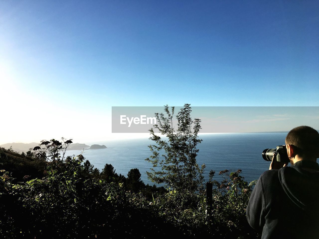 MAN PHOTOGRAPHING ON SEA AGAINST SKY