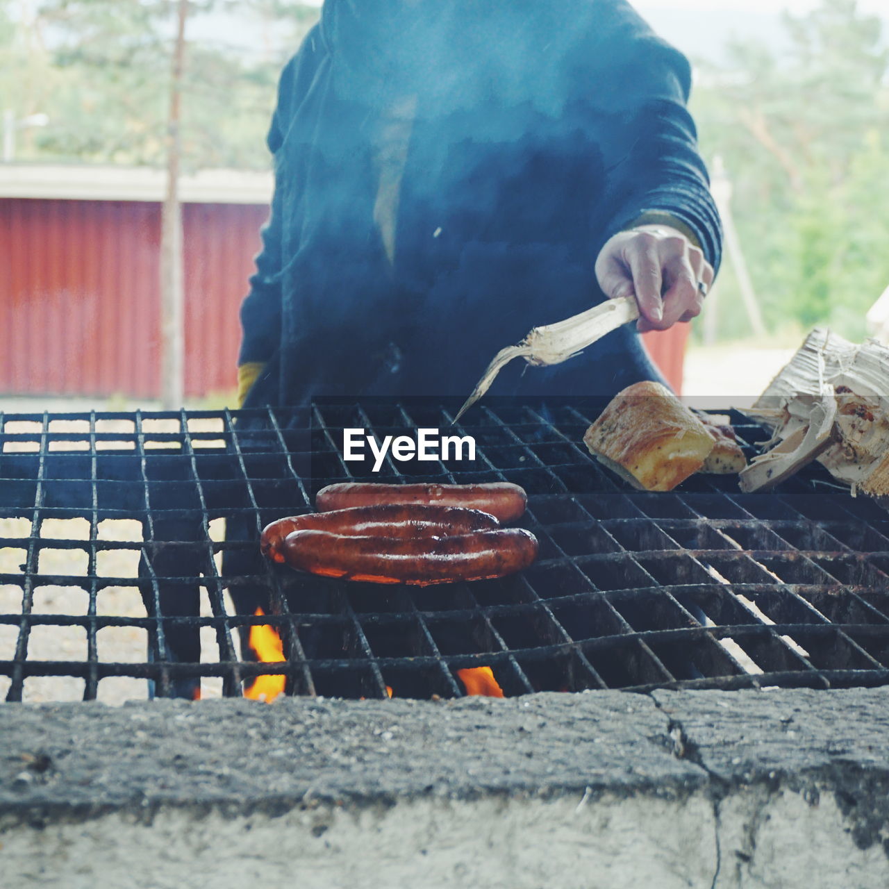 Midsection of man grilling sausages on barbecue at forest