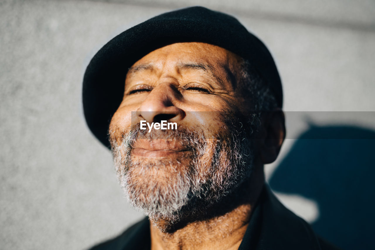 Smiling senior man with eyes closed against wall