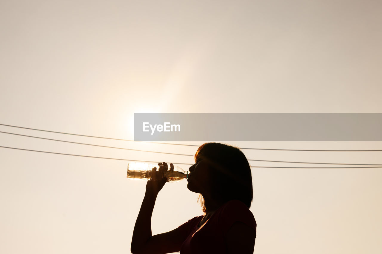 Side view of silhouette woman drinking against clear sky during sunset