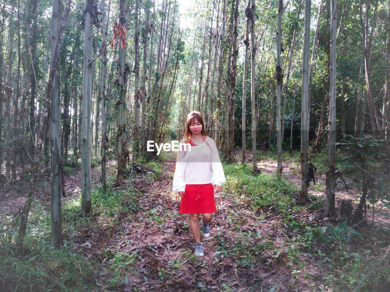 Full length of mid adult woman walking on field amidst trees in forest