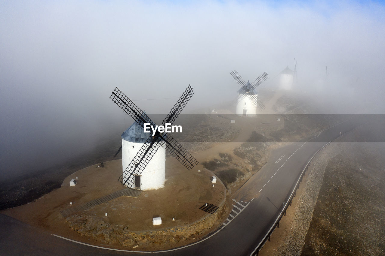 Spain, province of toledo, consuegra, aerial view of country road stretching past historical windmills during foggy weather