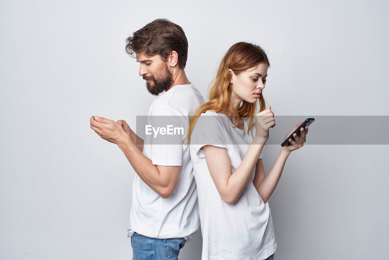 side view of smiling young woman using mobile phone against white background