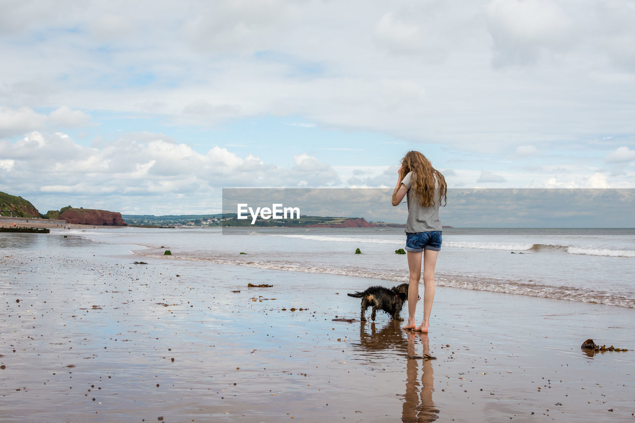 Rear view of girl with dog standing on shore at beach