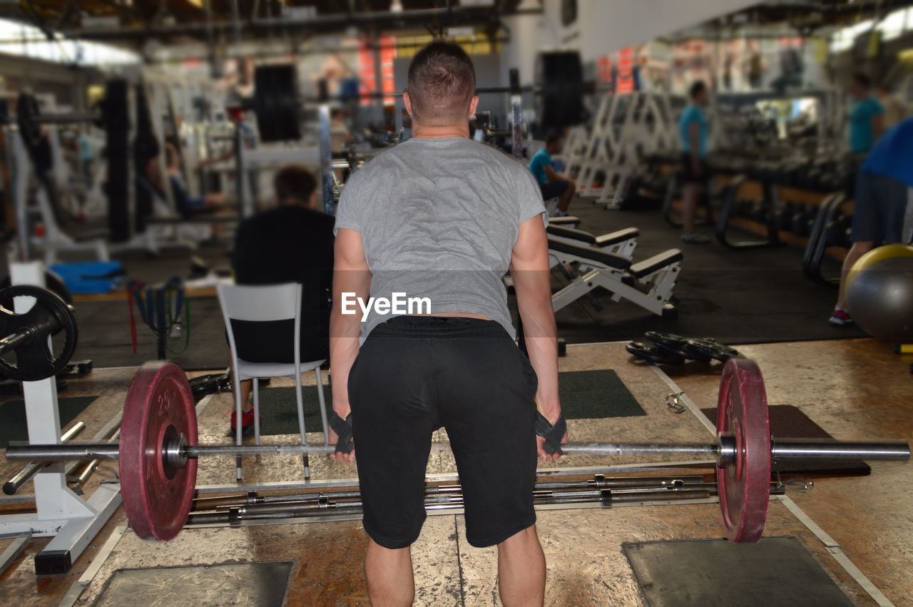 Rear view of mid adult man lifting weights in gym