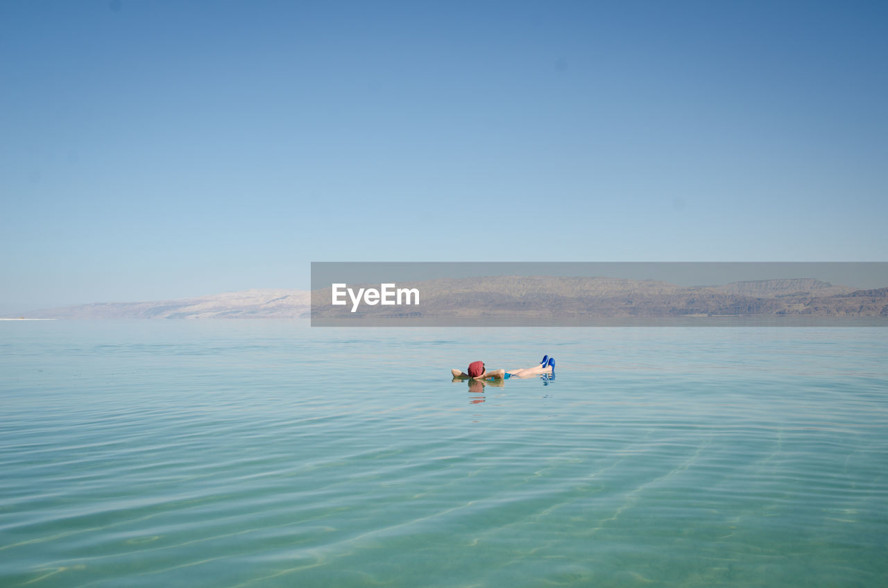 Man floating in dead sea against clear blue sky