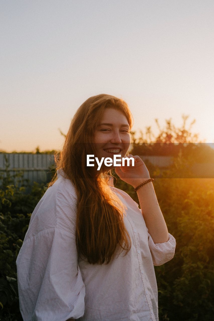 Smiling young woman standing against sky during sunset