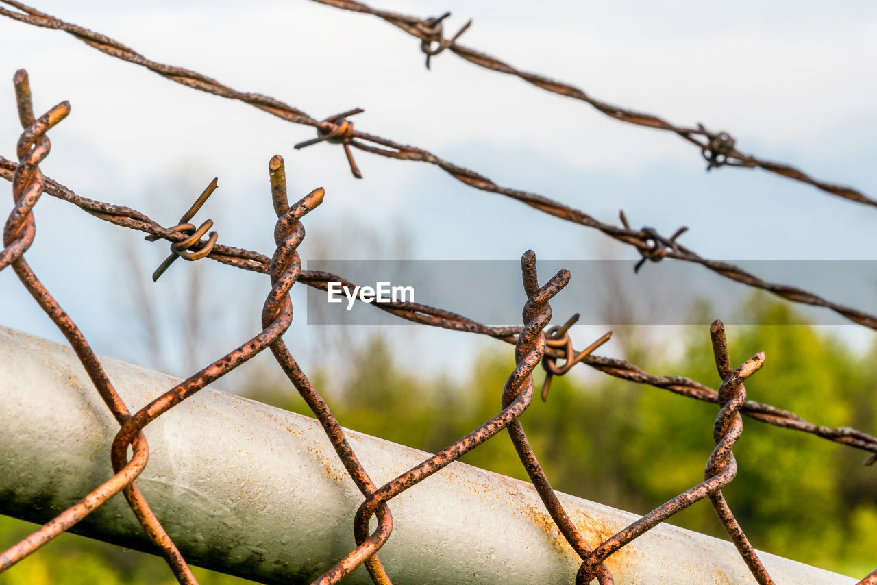 CLOSE-UP OF BARBED WIRE FENCE AGAINST BLURRED BACKGROUND