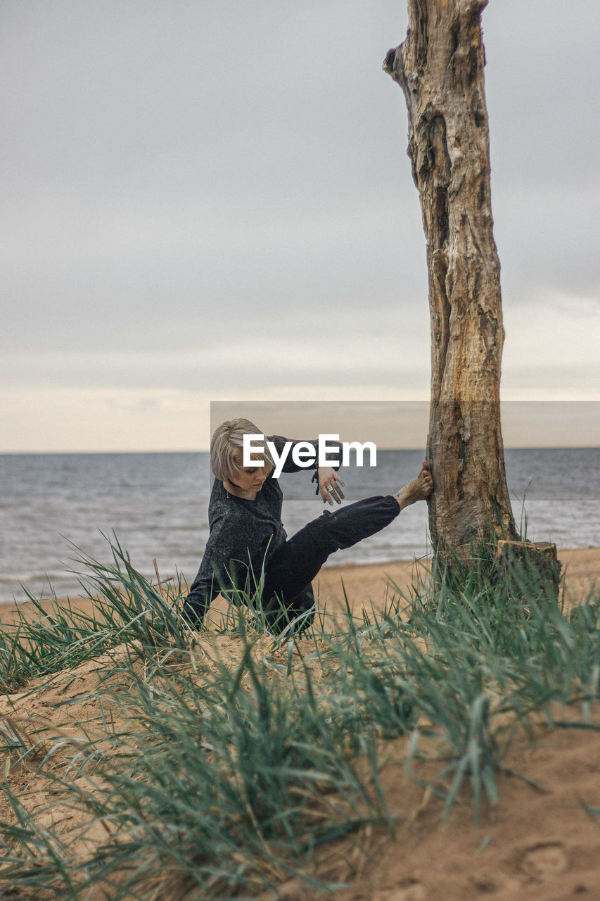 Young woman exercising while crouching by tree trunk at beach