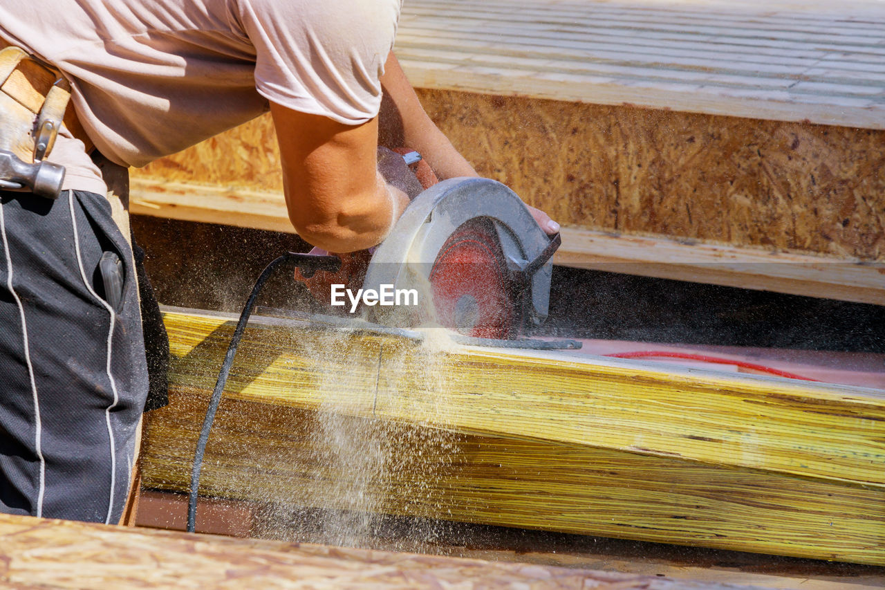 Midsection of man cutting wood at workshop