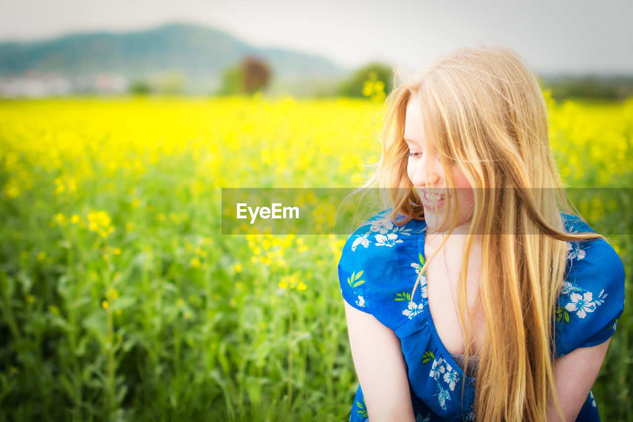 Smiling beautiful woman looking down against oilseed rape field