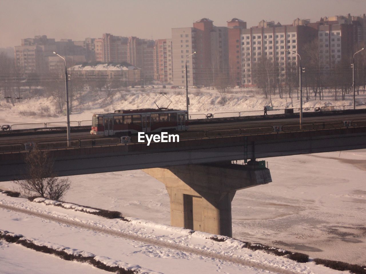 Bridge over frozen river in city against sky during sunset