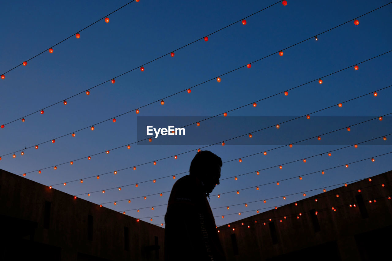 SILHOUETTE WOMAN STANDING AGAINST ILLUMINATED BLUE SKY