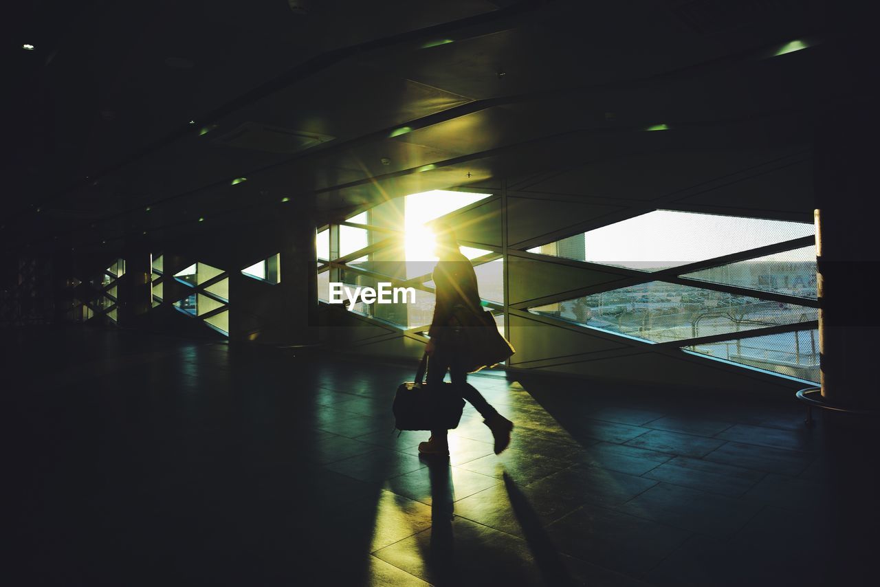 SILHOUETTE WOMAN WALKING ON ILLUMINATED WALKWAY