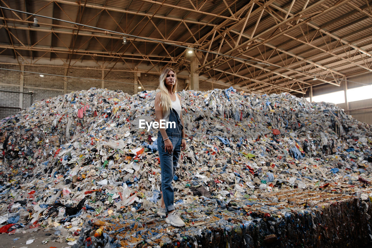 Portrait of young woman standing against garbage heap