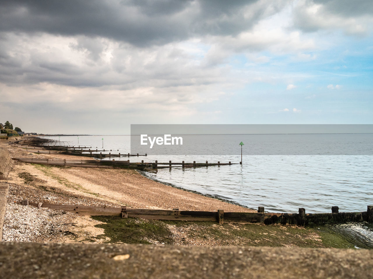 View of coastline at shoeburyness with no people, wooden groynes and storm clouds