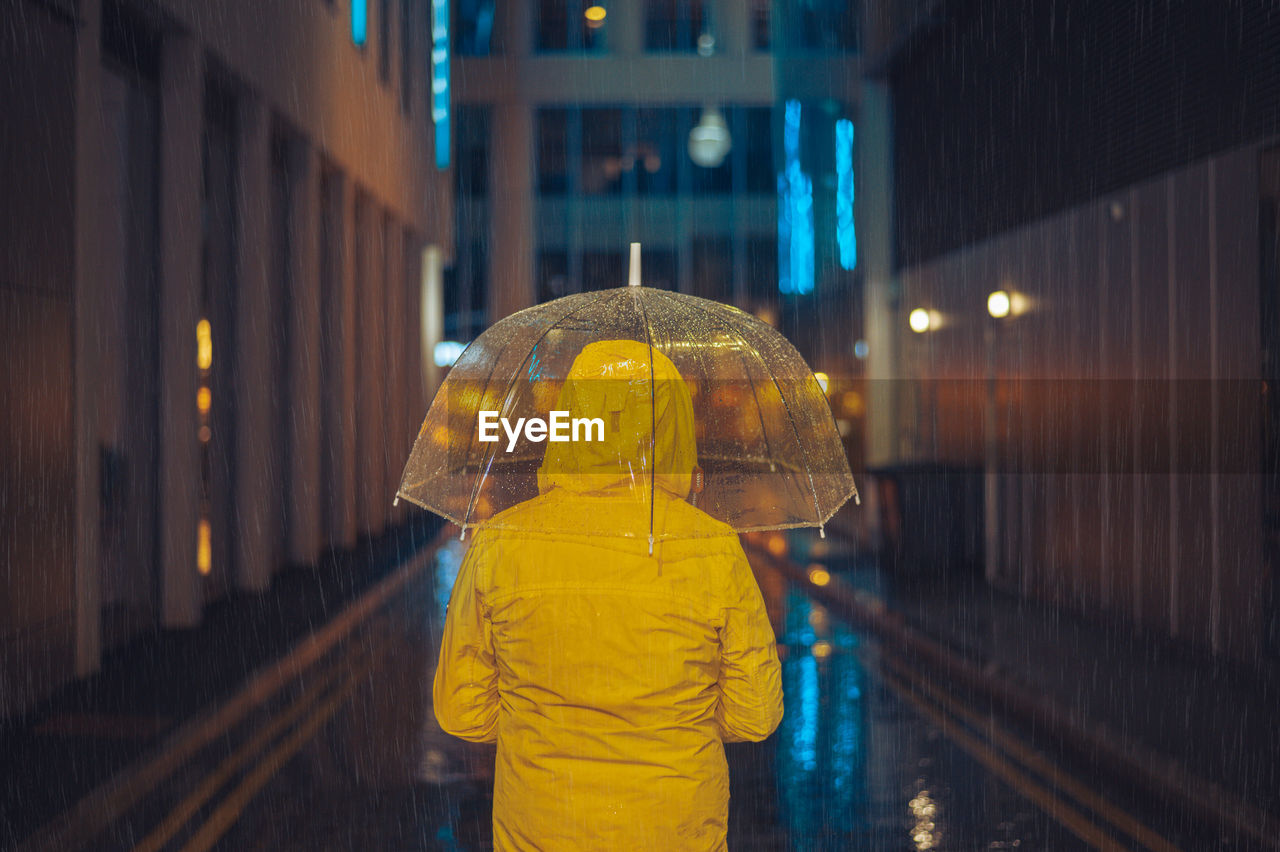 rear view of woman holding umbrella standing in city at night