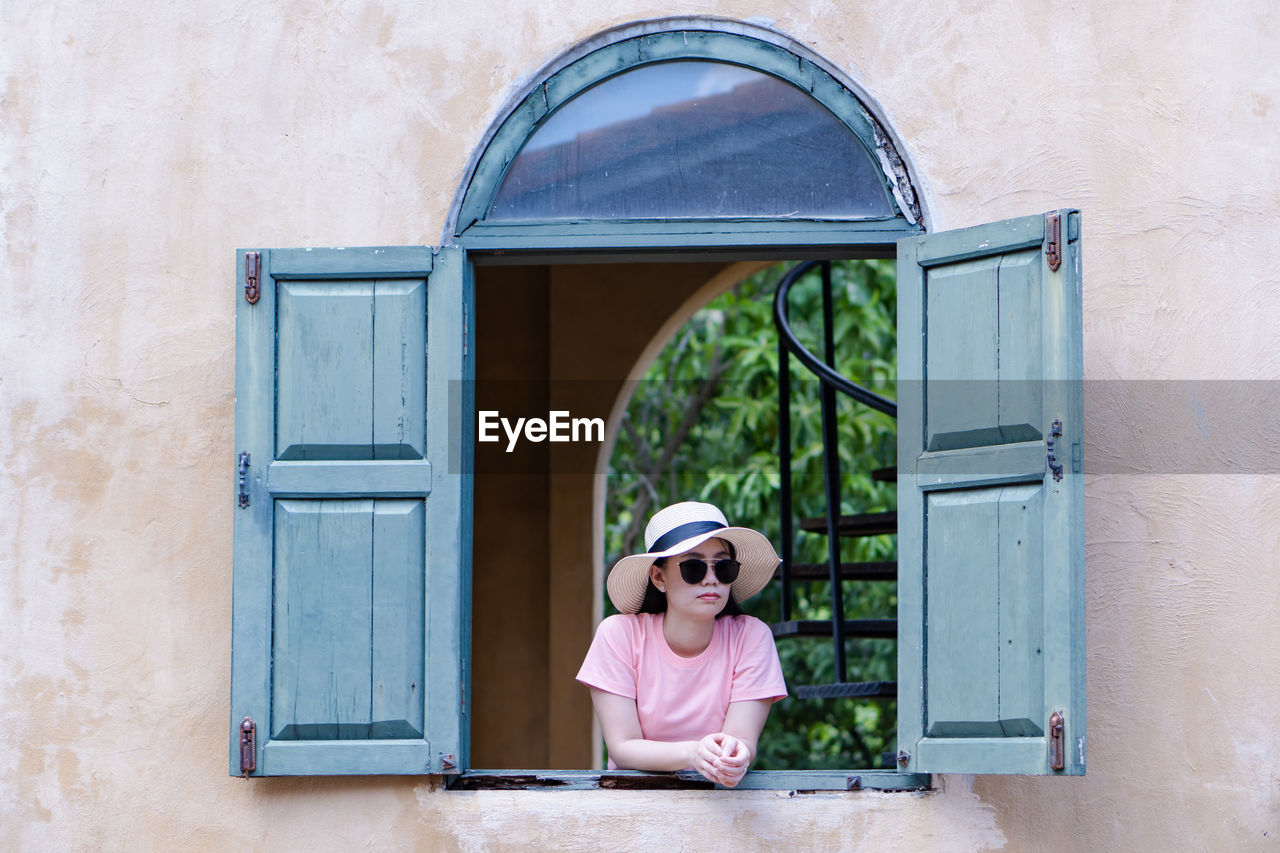 Woman in sunglasses standing at window of building